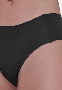 Mutande in cotone nero, stile bikini, con una texture liscia, vita alta e design minimalista, che mostrano una finitura senza cuciture.