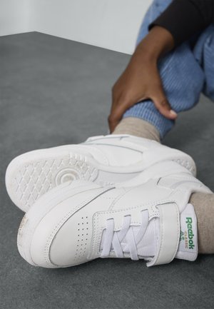 Balti Reebok sportbačiai su odiniu paviršiumi, raišteliais ir lipduku, tekstūruota padas ir žalia logotipų akcentai.