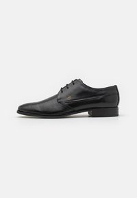 Scarpa da uomo in pelle nera con superficie texture, punta tonda e tre occhielli per i lacci. Presenta un tacco basso e piatto e un logo discreto.