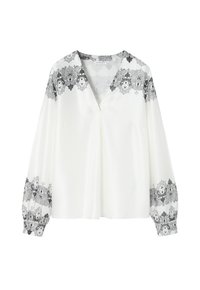 Blusa blanca con un escote en V pronunciado, mangas largas y un detalle de encaje floral negro en los hombros y los puños. Tela suave y ligera.
