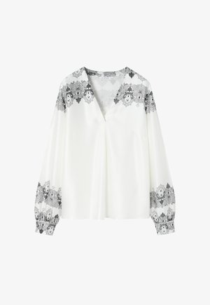 Weiße Bluse mit tiefem V-Ausschnitt, langen Ärmeln und schwarzem Blumen-Spitzenbesatz an den Schultern und Ärmeln. Glattes, leichtes Material.