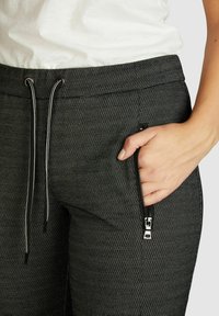 Joggers noirs en tissu tissé avec une finition texturée. Dotés d'une taille élastique à cordon de serrage et d'une poche latérale zippée avec quincaillerie en métal.