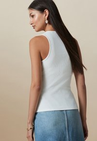 Débardeur blanc côtelé au design ajusté, avec bretelles et texture lisse. Assorti à une jupe en denim. Esthétique simple et épurée.