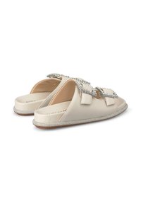 Scarpe beige slip-on con suola piatta, decorate con accenti di cristallo sulle cinghie e un bordo testurizzato lungo il perimetro. Design comodo e aperto.
