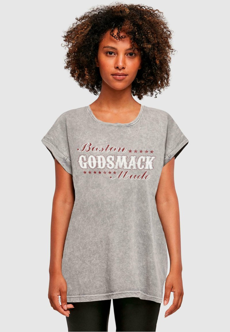 Pelēks, pārmērīgs T-krekls ar apaļu kakla izgriezumu, īsām piedurknēm un sarkanu tekstu "Boston GODSMACK Made" ar zvaigžņu akcentiem. Mīksta auduma tekstūra.