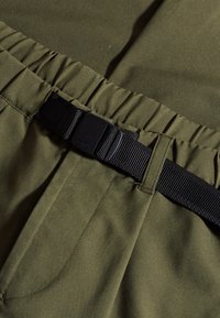 Olijfgroene broek met een geraffineerde tailleband, voorzien van een zwarte verstelbare webbingriem en details op de voorkant, gemaakt van soepel materiaal.