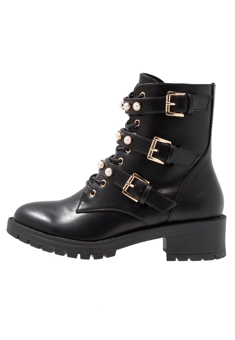 Bottine en cuir noir avec trois sangles ajustables, boucles dorées et accents décoratifs en perles. Talon épais noir et semelle crantée.