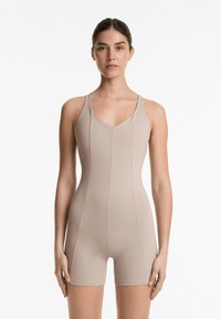 Beige lyhyet hihat bodysuit, jossa on v-pääntie, valmistettu sile�ästä kankaasta. Saumayksityiskohdat näkyvät edessä ja sivuilla.