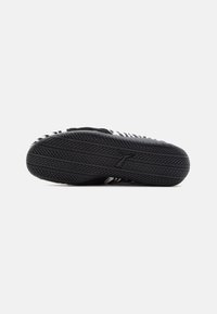 Black sneaker sole with textured rubber, featuring a distinctive tread pattern and a logo imprint. Upper displays a striped design.
