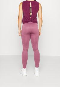 Sporttanktop i djupröd med en design med vriden rygg och meshpanel. Höga leggings i matchande nyans med texturerade detaljer. Vita sneakers.