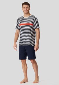 Men's striped T-shirt with navy and off-white horizontal stripes and a red accent stripe, paired with navy shorts. Cotton material, relaxed fit.