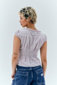 Bluza s smocanjem v pasu iz lahkega materiala s pastelno navpičnimi črtami, kratkimi naborki in nežnim volančkom okoli vratu. Ujemite jo z denim hlačami.