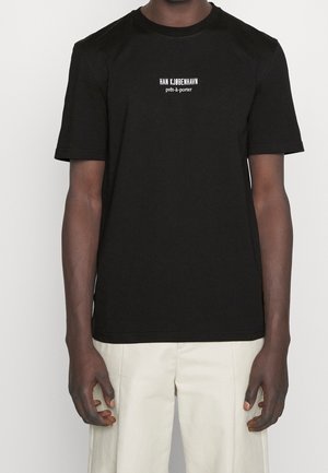 Black cotton t-shirt with short sleeves, featuring white printed text "HAN KJØBENHAVN prêt-à-porter" centered on the chest. Smooth texture.