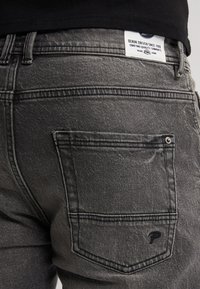 Grijze denim jeans met een vervaagde textuur, voorzien van een achterzak, stikseldetails en een label op de tailleband.