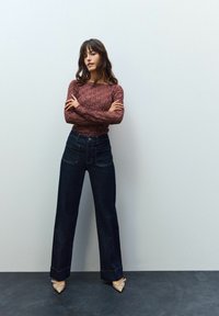 Bordeaux gebreide trui met een textuurpatroon, gecombineerd met donkerblauwe wijde denimjeans en puntige beige hakken.