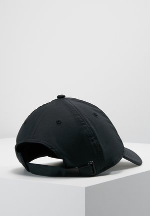 Czarna czapka bejsbolowa z regulowanym paskiem z tyłu, spoczywająca na białej powierzchni na tle jednolitego szarego tła.