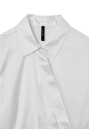 Blusa di raso bianco con colletto classico, dettaglio dei bottoni e texture liscia, caratterizzata da una piega verticale per un aspetto sartoriale. Etichetta del marchio visibile.