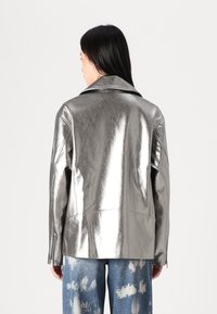 Metallisk sølvjakke med en strukturert design, bred krage og lange ermer; brukt med lyseblå slitte jeans.