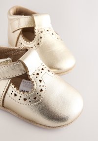 Chaussures bébé en cuir doré avec détails découpés, bout arrondi et bride à scratch. Semelle souple ; finition texturée.