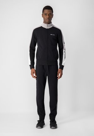 Tuta nera in tessuto morbido con giacca con zip caratterizzata da accenti grigi e logo, abbinata a pantaloni coordinati, che mette in mostra un design sportivo.