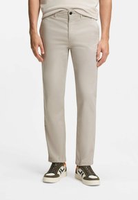 Beige Chinos mit schmaler Passform, ausgestattet mit Knopfverschluss und Fronttaschen, kombiniert mit grünen und weißen Sneakers. Strukturierter Stoff.