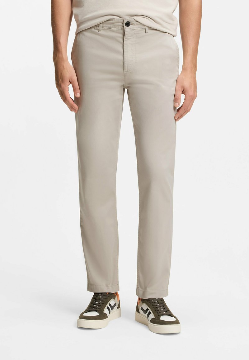 Beige Chinos mit schmaler Passform, ausgestattet mit Knopfverschluss und Fronttaschen, kombiniert mit grünen und weißen Sneakers. Strukturierter Stoff.