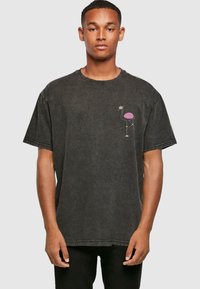 Camiseta de denim negro de manga corta, con un gráfico de flamenco rosa en la zona del pecho izquierdo y un diseño clásico de cuello redondo.