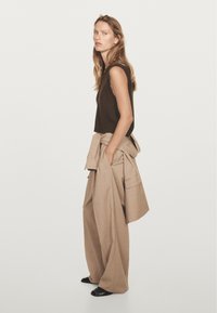 Brown sleeveless knit top paired with oversized beige trousers, featuring a belted waist and side pockets, worn with black shoes.