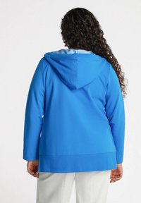 Una giacca blu con cappuccio realizzata in tessuto liscio, con un rivestimento interno a righe bianche e maniche lunghe con orlo dritto.