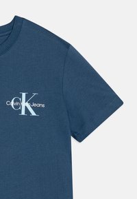 Zils īsām piedurknēm T-krekls, kas izgatavots no mīkstas kokvilnas ar ribotu apaļu apkakli. Krūtīs ir baltas krāsas apdruka ar tekstu "Calvin Klein Jeans".