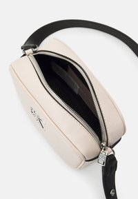 Vaaleanpunainen nahkainen olkalaukku, jossa musta hihna, hopeinen vetoketju, logoyksityiskohta ja tilava sisätila.