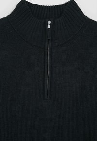 Maglione nero a maglia con colletto alto a costine e una chiusura lampo argentata corta. Tessuto testurizzato con una finitura liscia attorno alla zip.