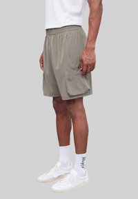 Lichtgrijze, lichte shorts met een elastische tailleband, zijzakken en een patchzak op het linkerbovenbeen. Katoenachtige textuur.