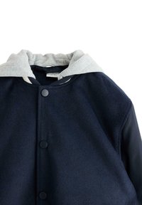 Marineblaue Wollmischung-Jacke mit hellgrauer Kapuze, Druckknopfverschluss und kontrastierenden Texturen an Körper und Ärmeln.