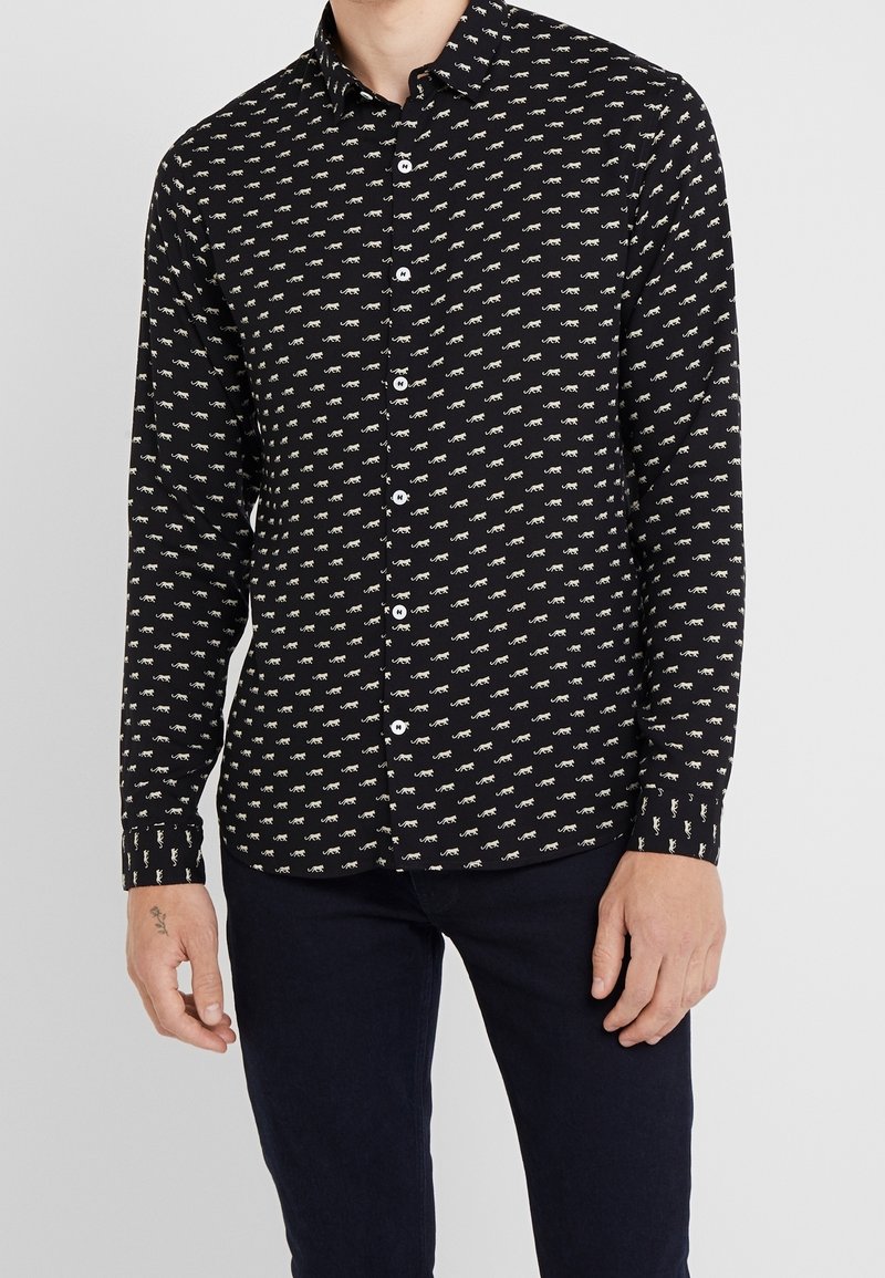 Camisa negra de botones con un estampado de animales blancos repetido, mangas largas y cuello estándar. La tela parece suave con un ligero brillo.