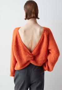 Suéter naranja de gran tamaño con un profundo escote en la espalda en V, que presenta un detalle de nudo en la cintura. Tejido suave y texturizado con mangas largas y sueltas.