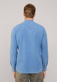 Camisa de manga larga azul claro hecha de tela de mezclilla, con un corte recto, cuello clásico y puños abotonados. Se muestra la vista posterior.