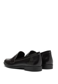 Mocassins en cuir noir avec une finition lisse, bout rond, style sans lacets et détails de couture subtils sur le dessus. Talon en caoutchouc bas.