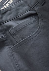 Ciemnoszary denim z tylną kieszenią z subtelnym przeszyciem. Materiał jest gładki, z klasycznym wzorem jeansów.