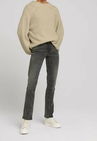 Beige stickad tröja med ribbat mönster, ihop med mörkgröna tajta jeans. Vita sneakers fulländar outfiten.