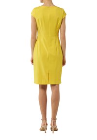 Gelbes kurzärmeliges Kleid mit taillierter Passform, knielang, Falten hinten und Reißverschluss. Getragen zu hautfarbenen High-Heels.