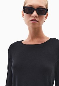 Czarny długi rękaw bluzka z prążkowanej tkaniny z okrągłym dekoltem. Czarne kwadratowe okulary przeciwsłoneczne dopełniają stylizację. Gładka faktura i luźny krój.