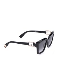 Lunettes de soleil carrées noires surdimensionnées avec verres dégradés foncés et fines charnières métalliques dorées sur fond blanc.