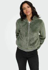 Zielona, pluszowa kurtka na zamek z kapturem, o miękkiej fakturze, z prążkowanymi mankietami i dołem oraz prostym wzornictwem.