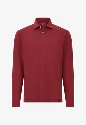 Dlhá svetločervená polo tričko s dvoma gombíkmi a malou čiernou nášivkou pri leme na jednofarebnom pozadí.