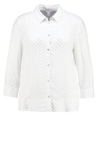 Vit långärmad blus med knapp-down krage, prydd med små gråa prickar, framknäppning och manschetter på ärmarna.