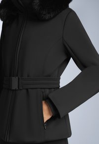 Crna jakna s krznom ovratnikom, pojasom u struku, bočnim džepovima i glatkom, teksturiranom tkaninom koja pruža toplinu i udobnost.