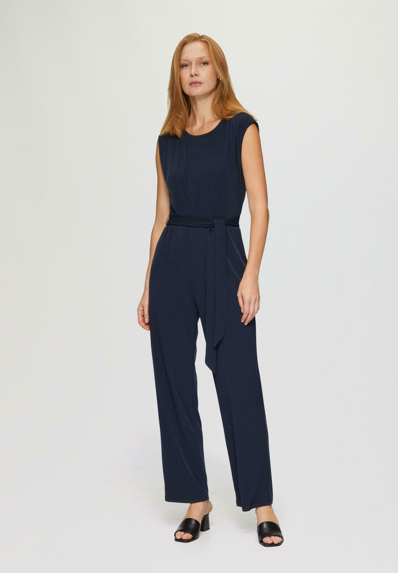 Marineblauwe jumpsuit met een aangesloten taille en een wijde pijpenontwerp. Voorzien van een ronde halslijn en een stoffen riem als accent. Glad textuur.