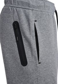 Primer plano de pantalones deportivos grises con dos bolsillos negros con cremallera y cintura con cordón.