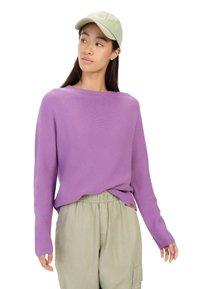 Lilla strikket sweater med lange ærmer, rund hals og sideskår, parret med en lys grøn kasket og beige cargo bukser med elastisk talje.